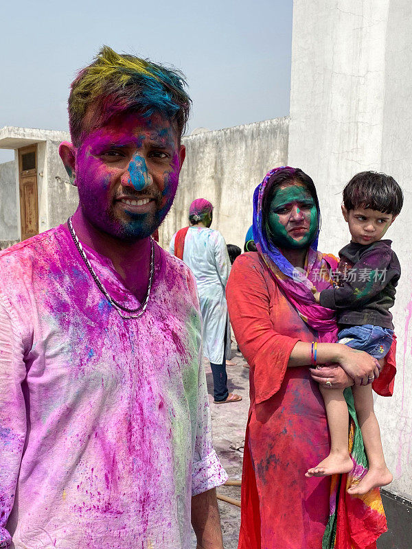 印度男女穿着Kurta和Salwar Kameez的传统服装，抱着年幼的女儿，身上覆盖着油漆粉颜色的gulal rang，在胡里节的色彩和爱漆战斗中嬉戏，微笑着看着相机